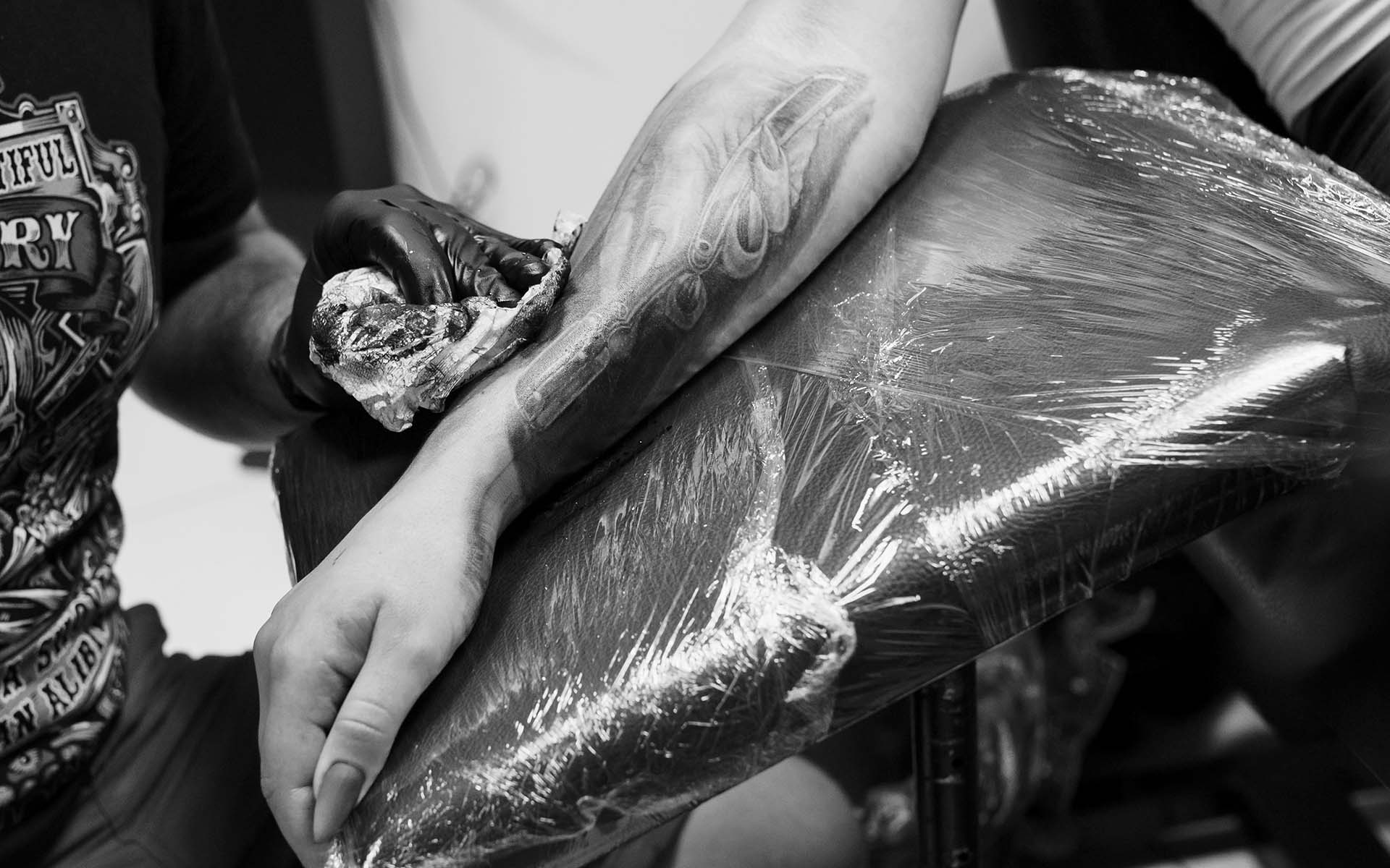 A tattoo artist works meticulously on a client's arm, showcasing a detailed tattoo design while cleaning the area.